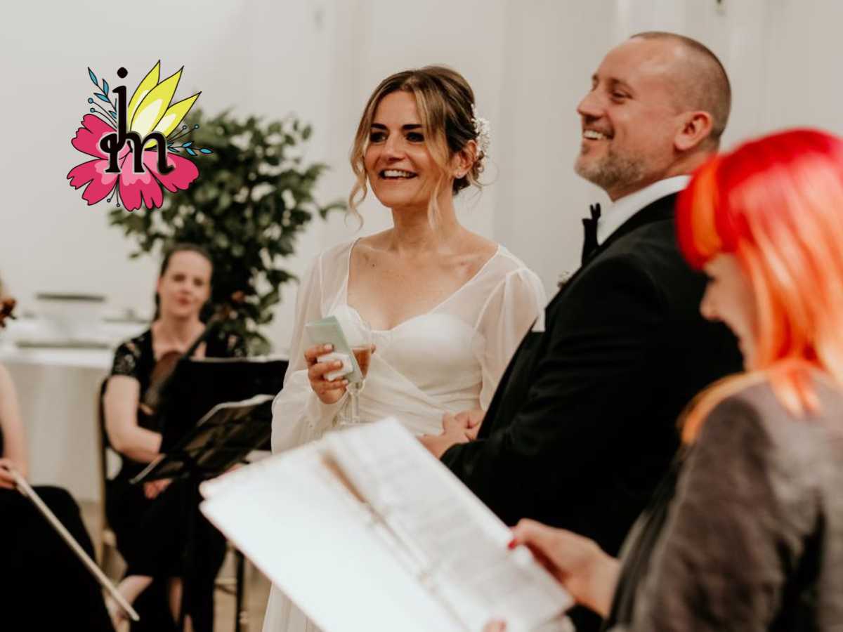A bride and groom. The bride is smiling and the groom is laughing. the light is white and bright, there is someone reading from a folder you can see the back of her head and her hair is orange.