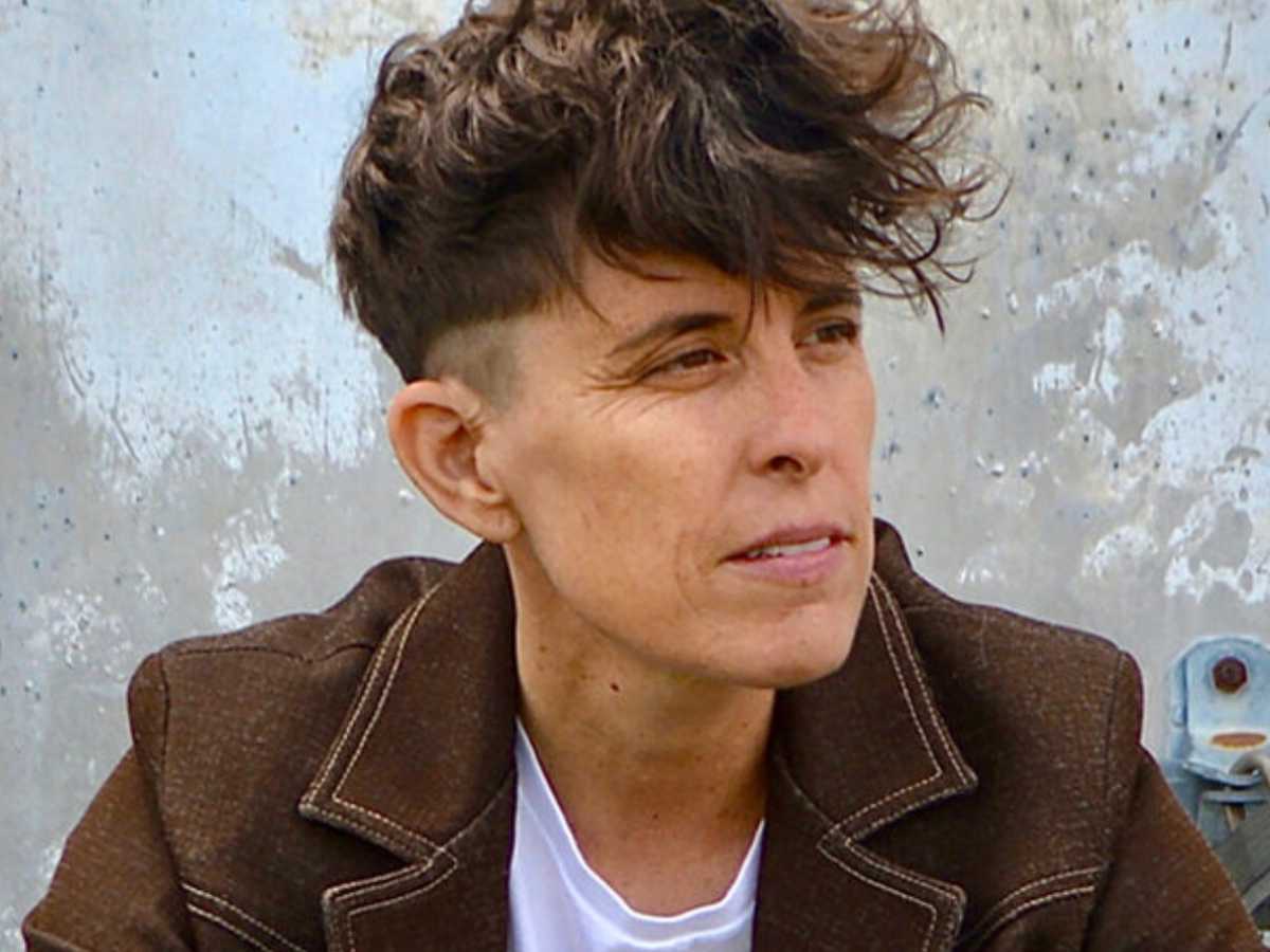 Wedding Ceremony unique readings A non-binary person with dark hair and tanned skin looking to their left in a dark brown jacket.