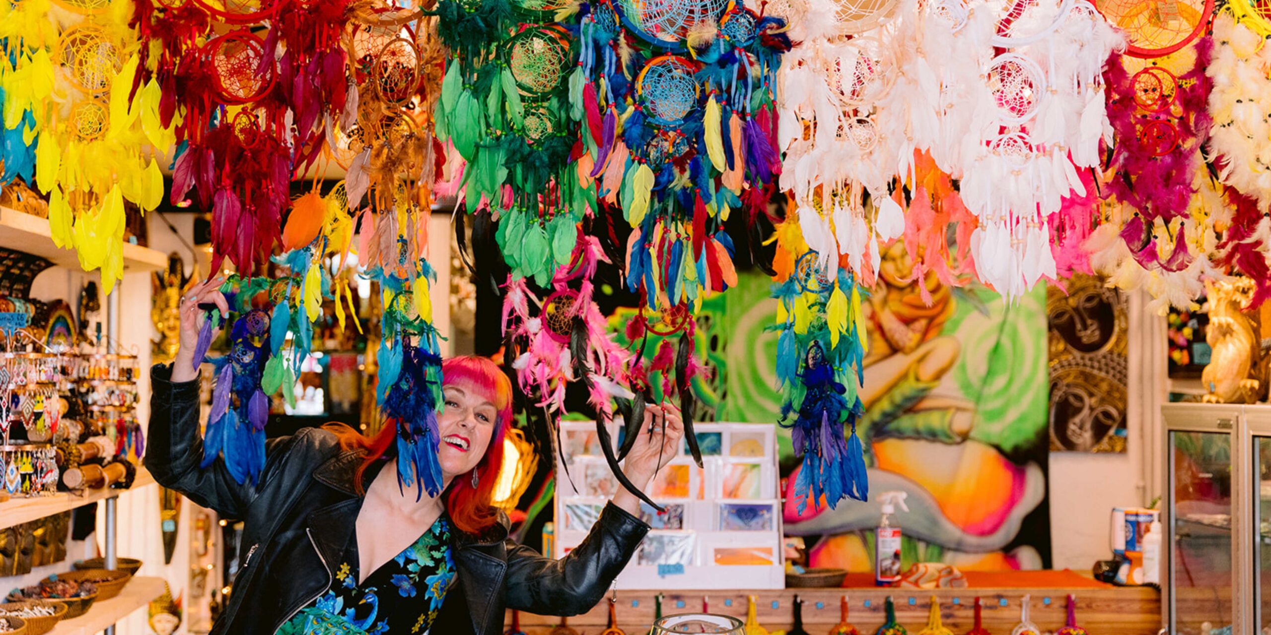 polyamorous wedding ceremonies Jess May peering through a curtain of multi coloured feather dream catchers