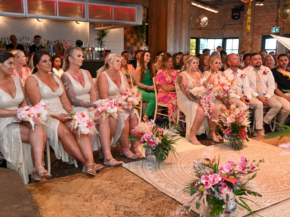 wedding readings A gathering of wedding guests at a wedding ceremony. Everyone is smiling, everyone is white and they all have tans and are quite contemporary in appearance.