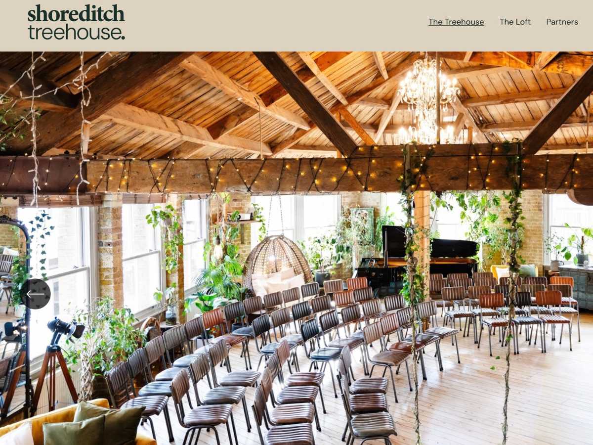 The Shoreditch Tree House Unusual-London-wedding-venue A gorgeous image of a ceremony space set up in a tree house with a swing and curved rows of seats. Plants are everywhere and the light is beautiful. there are fairy lights and in the corner there is a logo for The Shoreditch Tree house