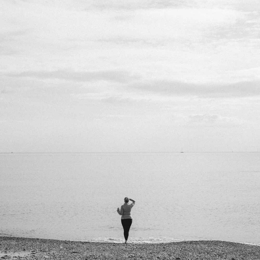 A figure in black and white staring out to sea