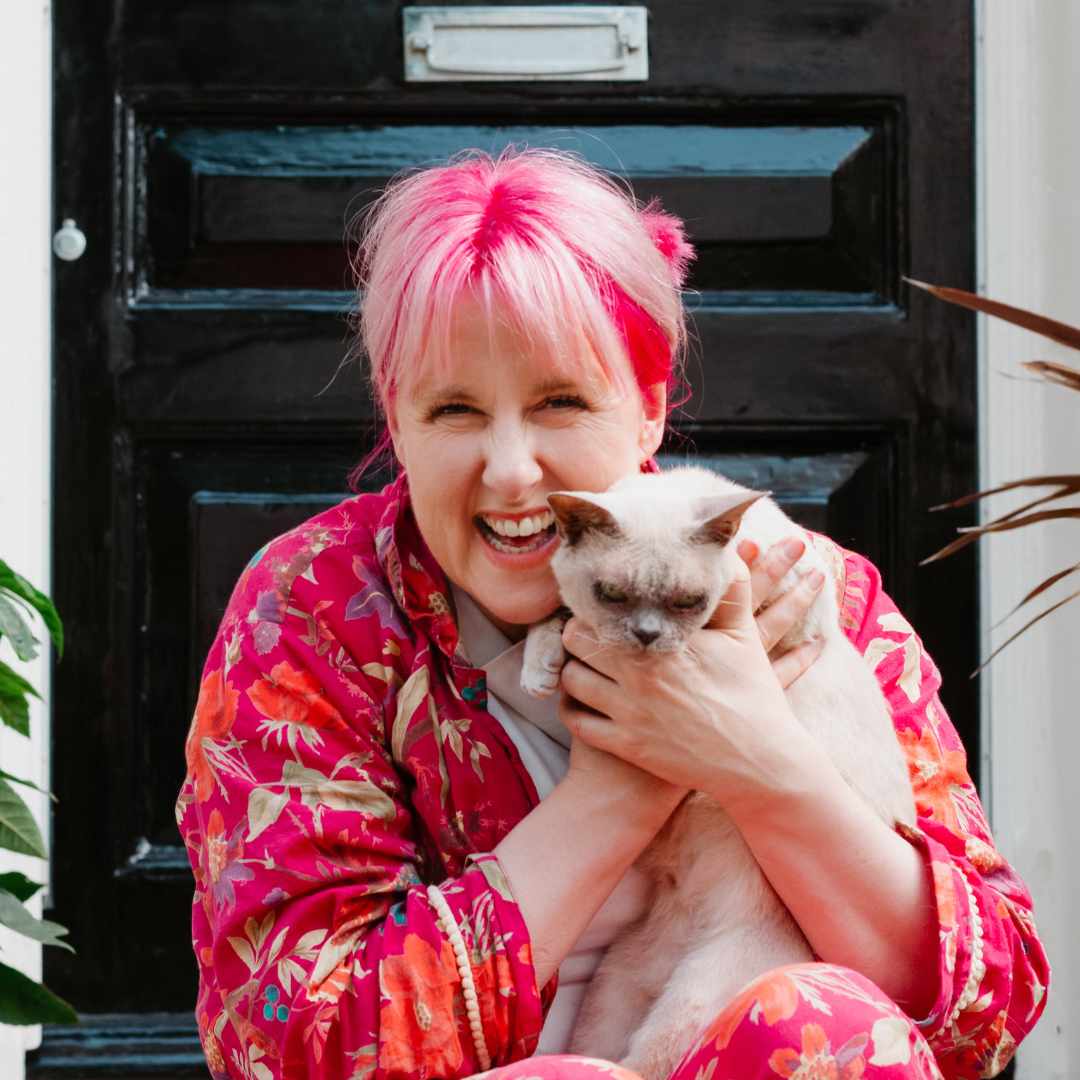 newly engaged couples Jess May with pink hair holding a cat and laughing, wearing her pyjamas on her doorstep sat in front of a shiny black door.