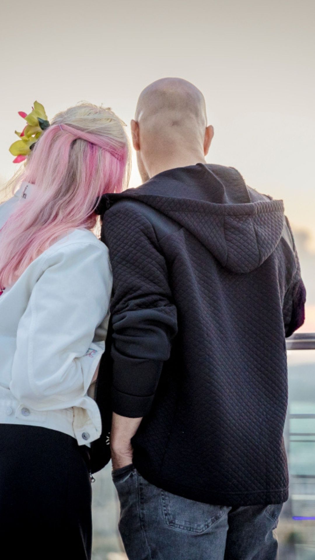 Jess May Celebrant in Brighton (1) A man and a woman look out to sea together. He has a shaved head and she has pink hair with flowers.